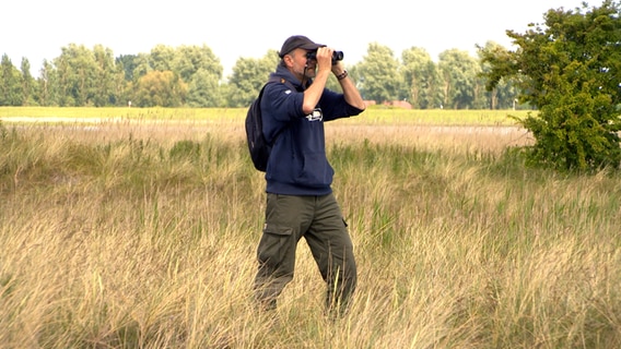 Vogelwart Carsten Harrje blickt im Naturschutzgebiet Bottsand (Kreis Plön) durch ein Fernglas © NDR Foto: NDR