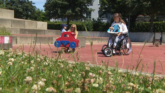 Zwei Frauen, die eine der beiden im Rollstuhl, sitzen auf einem Kinderspielplatz © NDR Foto: NDR