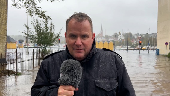 Andreas Rackow steht in Flensburg vor einer überschwemmten Stadt. © NDR 