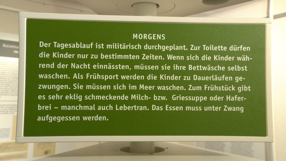 Ein Schild beschreibt den Tagesablauf in einem Kurheim für Kinder. Der Text lautet: Morgens - Der Tagesablauf ist militärisch durchgeplant. Zur Toilette dürfen die Kinder nur zu bestimmten Zeiten. Wenn dich die Kinder während der Nacht einnässten, müssen sie ihre Bettwäsche selbst waschen. Als Frühsport werden die Kinder zu Dauerläufen gezwungen. Sie müssen sich im meer waschen. Zum Frühstück gibt es sehr eklig schmeckende Milch- bzw. Griessuppe oder Haferbrei - manchmal auch Lebertran. Das Essen muss unter Zwang aufgegessen werden. © NDR Foto: Sven Jachmann