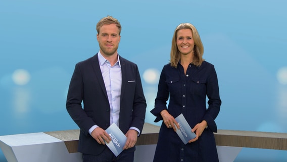 Moderator Henrik Hanses und Moderatorin Gabi Lüeße stehen im Studio des Schleswig-Holstein Magazins vor dem Pult nebeneinander. © NDR 