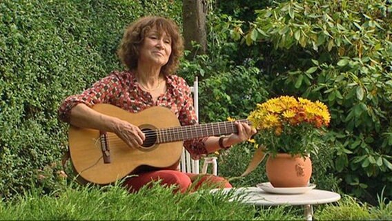 Eine Frau sitzt in einem Garten und spielt Gitarre © NDR 
