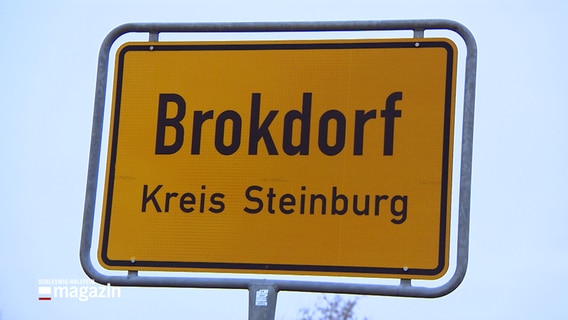 Das gelbe Ortsschild von Brokdorf steht vor grau-blauem Himmel. © NDR 