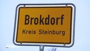 Das gelbe Ortsschild von Brokdorf steht vor grau-blauem Himmel. © NDR 