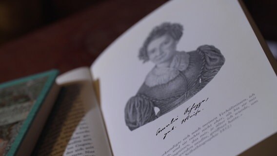 Ein aufgeschlagenes Buch zeigt das gemalte Bild einer Frau. © NDR / Zeitreise 
