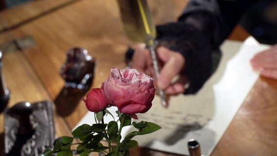 Eine Frau schreibt mit Feder und Tinte im Hintergrund einer Rose. © NDR / Zeitreise 