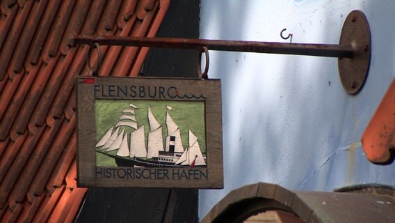 Ein altes Schild mit Überschrift "Flensburg Historischer Hafen" hängt über einem Hauseingang. © NDR 