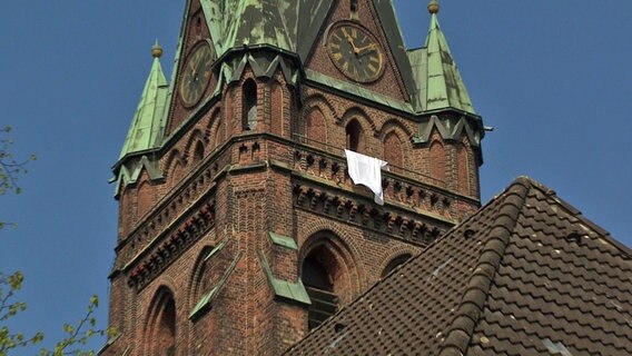 An einem Kirchturm hängt ein weißes Laken.  