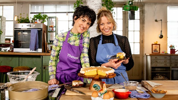 Zora Klipp und Theresa Knipschild stehen vor einem Orangenkuchen in einer Küche. © NDR Foto: Claudia Timmann