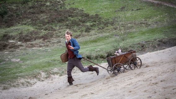 Hans (Anton Spieker) ist mit seinem getauschten Schwein im Bollerwagen im Glück. © NDR/Georges Pauly 