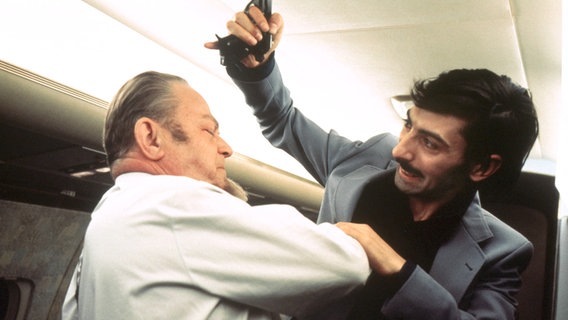 Brutal schlägt Femal Racadi (Joe Bogosyan) einem älteren Fluggast (Willy Krüger, links), der die bedrohte Stewardess befreien will, seine Pistole über den Kopf. © NDR/Edda Sachs 