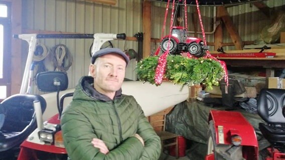 Sven Tietzer in einer Scheune mit Trecker-Adventskranz. © NDR 