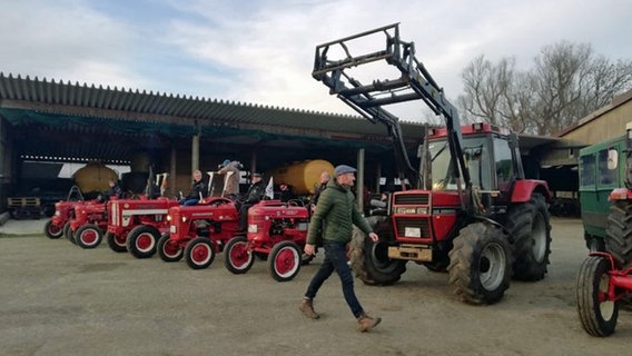 Sven Tietzer läuft an vielen roten Traktoren vorbei. © NDR 