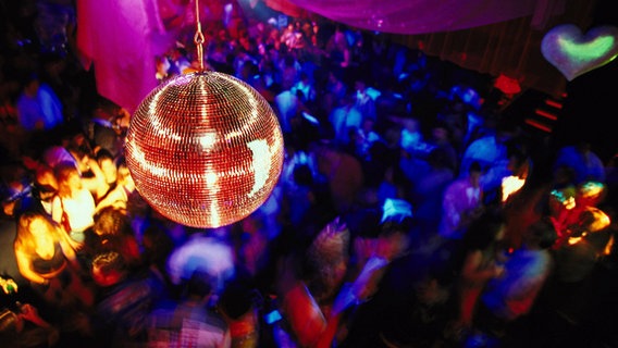 Eine Discokugel hängt in einem Club über tanzenden Menschen. © picture alliance 