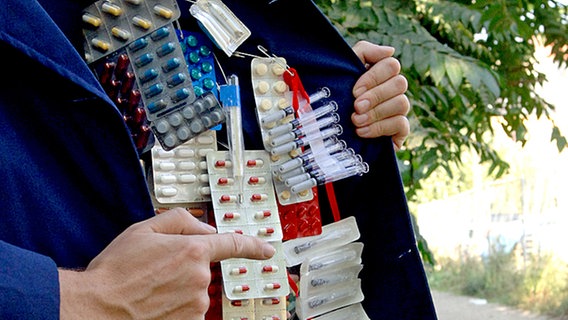 Dealer mit geöffnetem Mantel und Arzneimitteln © Bundesvereinigung Deutscher Apothekerverband Foto: El Pato