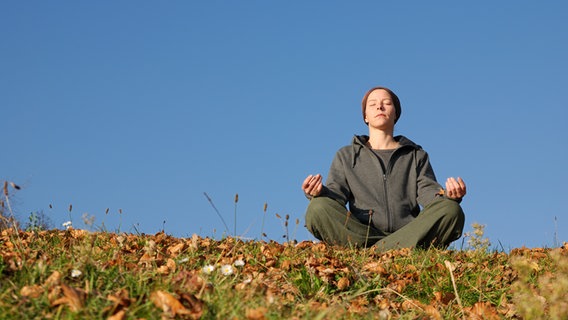 Frau sitzt im Lotusitz auf einer herbstlichen Wiese. © fotolia Foto:  gradt