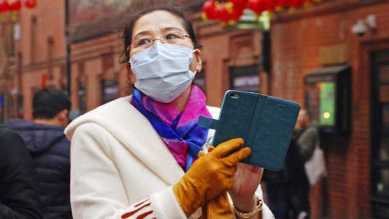 Eine asiatische Frau trägt einen Mundschutz. © Photoshot 