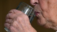 Eine ältere Frau führt ein Glas Wasser zum Mund. © picture alliance Foto: Sebastian Willnow