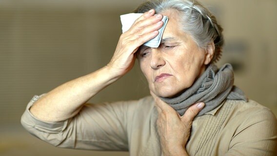 Frau mit Hals- und Kopfschmerzen hält sich ein Taschentuch an die Stirn. © Colourbox 
