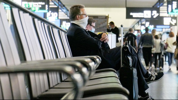 Ein Mann mit Mund-Nasen-Bedeckung sitzt in einer Flughafen-Abfertigungshalle. © picture alliance / NurPhoto Foto: Nicolas Economou
