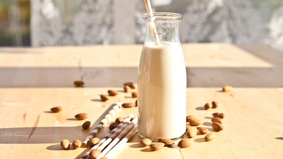 A glass bottle with a straw stands on a table with almonds and straws on it.  © picture alliance/chromorange Photo: Barbara Neveu