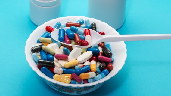 Eine Schüssel voller Tabletten, darüber ein Löffel gefüllt mit Medikamenten. © colourbox 