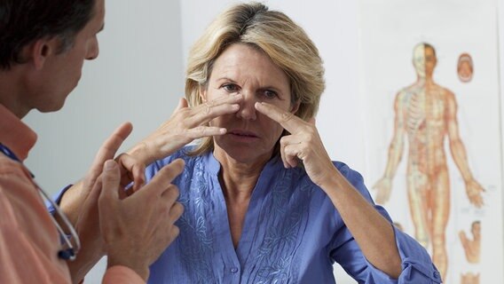 Eine ältere Frau deutet auf ihre Nase. Vor ihr steht ein Arzt. © phantermedia Foto: imagepointfr
