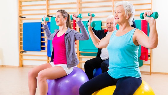 Two seniors train with a trainer with small dumbbells on exercise balls.  © Colourbox photo: Kzenon