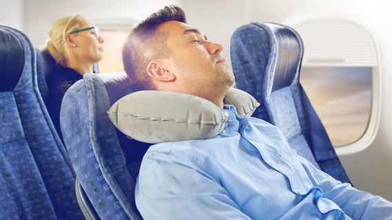 Ein Mann schläft mit einem Nackenkissen im Flugzeug. © Colourbox Foto: Syda Productions