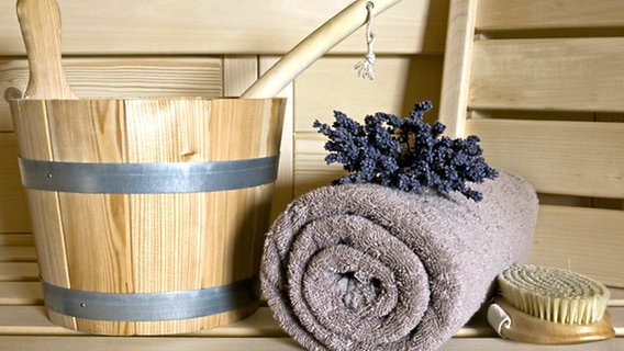Massagebürste, Handtuch und Aufgusseimer auf einer Saunabank © Panter Media Foto: Michaela Pucher
