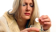 Eine Frau mit schmerzverzerrtem Gesicht löst eine Schmerztablette in einem Glas Wasser auf. © dpa Foto: Heiko Wolfraum