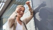 Eine Frau greift sich im Stehen an die Stirn, stützt sich an der Wand ab und schließt die Augen. © picture alliance Foto: Christin Klose