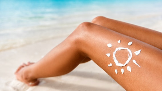 Sonnensymbol ist mit Sonnencreme auf ein Bein einer Sonnenbadenden gemalt. © Fotolia.com Foto: Maridav