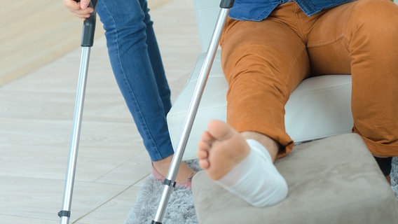 Ein Mann sitzt zu Hause mit einem verletzten Bein und Krücken. © Colourbox Foto: Phovior