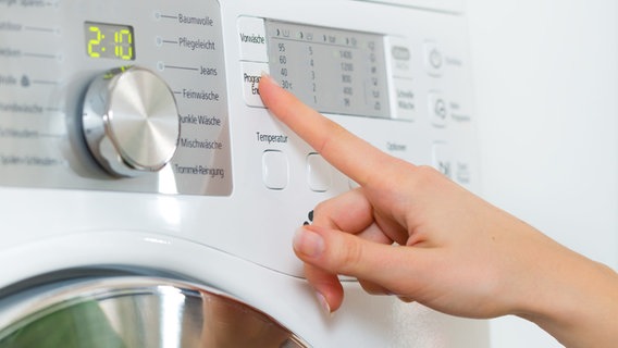 Mann sieht die Hand einer Frau, die die Programmwahltaste einer Waschmaschine drückt. © colourbox Foto: Kzenon