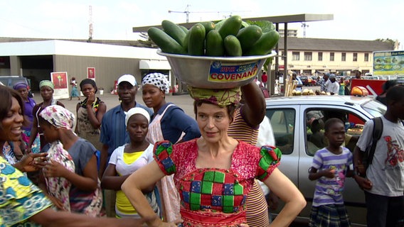ARD Korrespondentin Sabine Bohland trägt Gemüse in einer Schale auf dem Kopf  