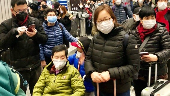 Menschen mit Mundschutz am Flughafen in Peking.  