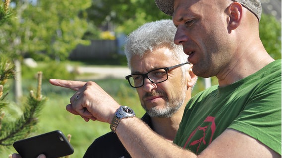 Clas Oliver Richter und Kameramann Mathias schauen auf ein Smartphone.  