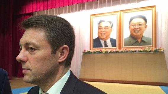 Korrespondent Uwe Schwering vor zwei Bildern der ehemaligen Machthaber Nordkoreas.  