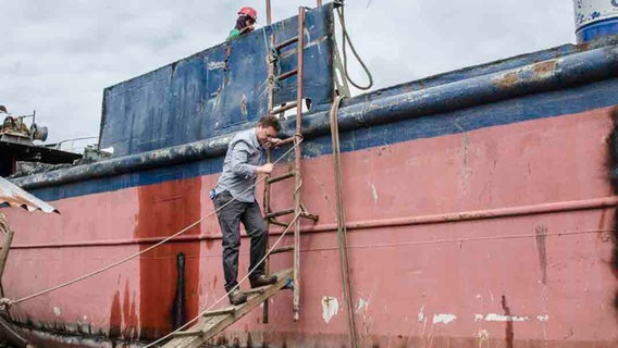 Korrespondent Uwe Schwering klettert an einer Leiter ein altes Schiff herunter  