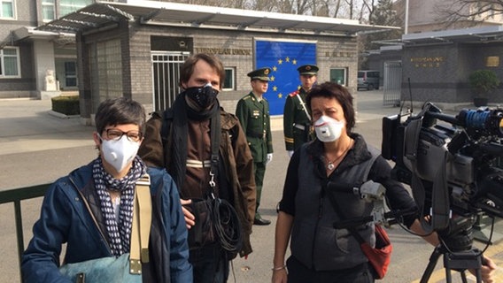 Sascha Storfner, Tonmann Kristian Baum und Kamerafrau Karin Kresel (v.l.n.r.) vor der EU Botschaft in Peking. Sie alle tragen Atemschutzmasken.  