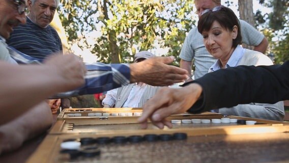 ARD-Korrespondentin Birgit Virnich schaut Männern beim Backgammonspielen zu.  