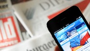 Tageszeitungen und ein Smartphone mit der Tagesschau-App. (Illustration) © dpa Foto: Julian Stratenschulte