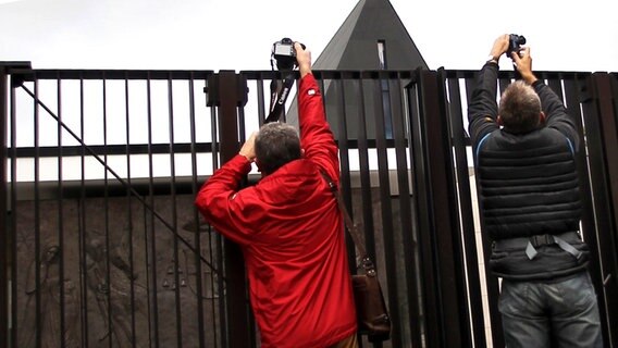 Zwei Journalisten fotografieren die Kapelle des Bischofshauses in Limburg über einen Zaun hinweg. ©  picture alliance / dpa Foto: Fredrik Von Erichsen