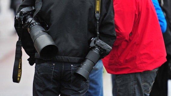 Einem Mann hängen zwei Kameras über seinen Schultern. © picture alliance / maxppp Foto:  CLAUDE PRIGENT
