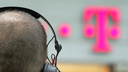 Ein Journalist steht mit Kopfhörer vor einem Logo vor der Konzernzentrale der Deutschen Telekom in Bonn (c) dpa - Bildfunk, Foto: Rolf Vennenbernd © Rolf Vennenbernd Foto: Rolf Vennenbernd