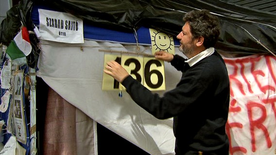 Der ungarische Journalist hängt die Zahl 136 an sein Zelt © NDR 