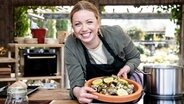 Chef Zora Klipp stands at the counter in her outdoor kitchen and holds a tagine in her hand.  © NDR Photo: Claudia Timmann