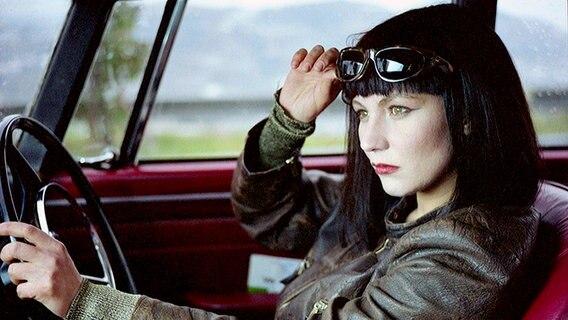 Claire Tourneur (gespielt von Solveig Dommartin) sitzt am Steuer eines Autos. Sie schiebt eine Sonnenbrille auf ihren Kopf. Sie hat eine schwarze Bob-Frisur mit Pony und trägt eine braune Lederjacke. © picture alliance / dpa | zdf/arte 