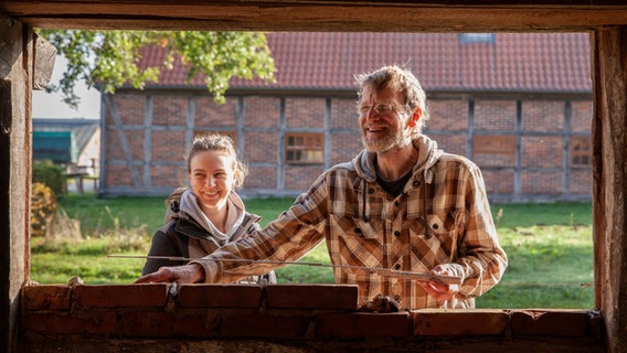 Eine junge Frau und ein älterer Mann bauen an einer alten Scheune eine Mauer. © NDR/Kamera Zwei 